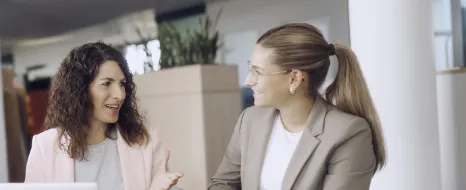 Zwei Kolleginnen unterhalten sich an einem Schreibtisch in einem Büro.