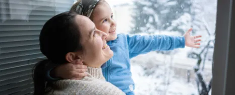 Eine Mutter hat ihr kleines Kind auf dem Arm und beide schauen aus dem Fenster. 