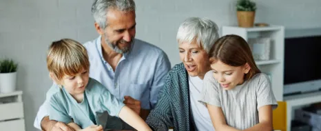 Ein älteres Paar spielt mit seinen Enkeln und denkt über die beste Möglichkeit nach, monatlich Geld für diese anzulegen.