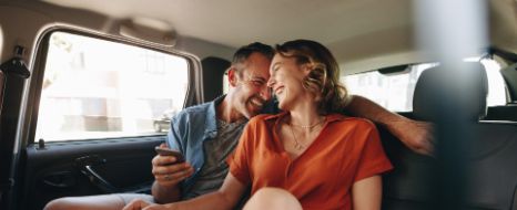 Mann und Frau lachen auf der Rückbank eines Autos.