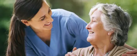 Pflegerin lächelt eine alte Dame an die sie zurück anlächelt.