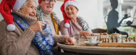 Mehrere alte Personen haben eine Weihnachtsmütze auf und sitzen gemeinsam an einem Tisch und trinken dort Tee.