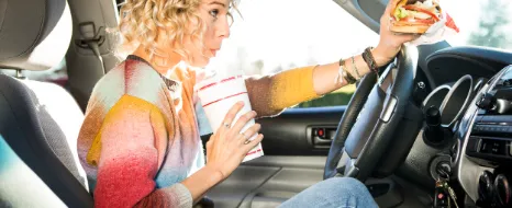 Junge Frau isst Fastfood am Steuer.