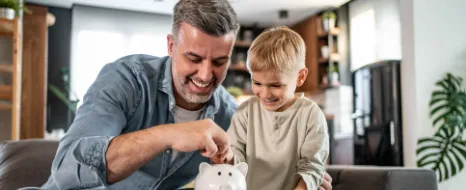 Ein Junge legt Münzen in ein Glas als Symbol für das Kindergeld, dass seine Eltern für ihn anlegen konnten. 