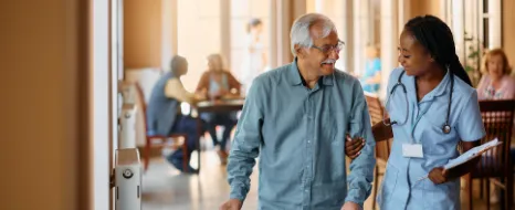 Freundliche Krankenschwester die einem aelteren Mann bei der Verwendung von Mobilitaetshilfen im Pflegeheim hilft