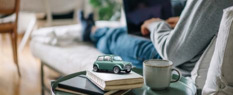 Person sitzt mit Kaffee und Laptop auf dem Sofa.