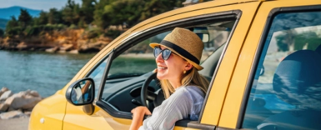 Eine Frau mit einer Sonnenbrille sitzt im Auto und schaut aus dem Fenster in Richtung Meer . 