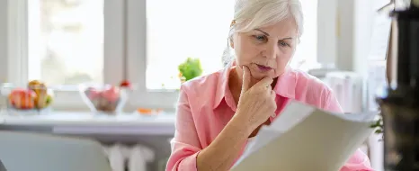 Seniorin verfasst Vollmacht mit Laptop und Dokumenten am Kuechentisch bei sich zu Hause