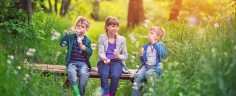 Kinder machen Seifenblasen in der Natur und fühlen sich sicher, weil ihre Eltern an die Kinderabsicherung gedacht haben.
