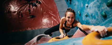 Frau klettert eine Indoor-Kletterwand hoch.