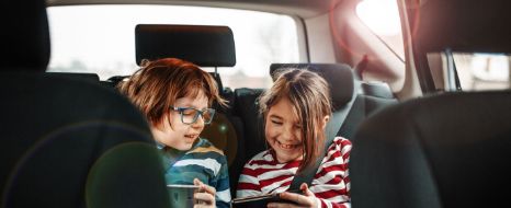 Geschwister spielen am Smartphone im Auto.