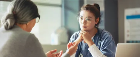 Beratungssituation mit Pflegerin und Seniorin am Tisch mit Papieren und Klemmbrett