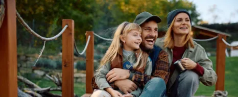 Mutter, Vater und Tochter sitzen auf einem Bootssteg und beschäftigen sich mit der Frage, was ein Kind bis zum 18. Lebensjahr kostet. 