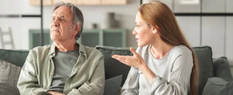 Tochter redet gestikulierend auf älteren Mann ein der ernst in die andere Richtung blickt