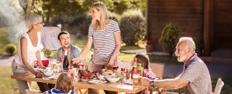 Eine Familie sitzt fröhlich im Garten beim Essen.