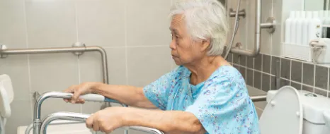 Eine alte Frau stuetzt sich im Badezimmer auf Sicherheitsgriffe