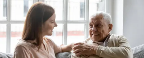 Pflegekraft sitzt nah an Senior und berührt ihn liebevoll an Schulter