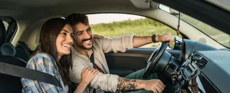 Ein Mann und eine Frau fahren im Auto. Sie lachen und sie berührt ihn am Arm.