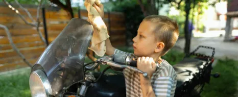 Motorrad waschen: Ein Kind reinigt ein Motorrad mit einem Tuch.