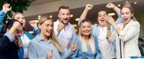Jubelnde Nachwuchskräfte spielen gemeinschaftlich Tischfußball und genießen eine entspannte Pause in einem modernen Büro.