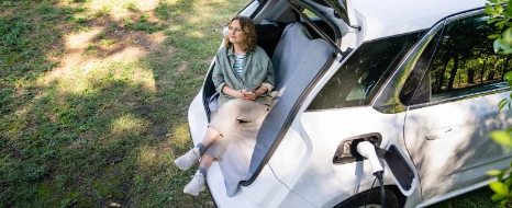 Eine Frau lädt ihr Elektroauto während sie im Kofferraum sitzt und wartet.