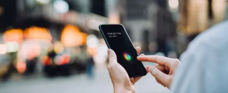 Person hält Smartphone in der Hand und benutzt Sprachassistenten.