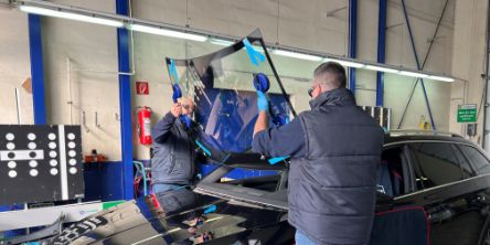 In einer Autowerkstatt setzen zwei Männer eine neue Windschutzscheibe ein.