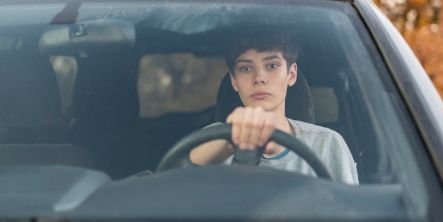Ein junger Teenager sitzt im Auto und lernt Autofahren.