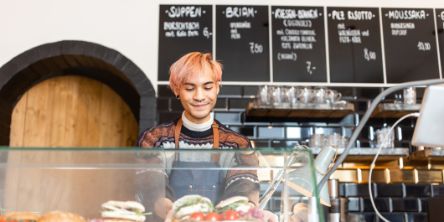 Junger Barista, der frisch zubereitete Speisen in der Auslage eines Cafés anrichtet.