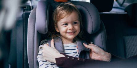 Ein Mädchen sitzt im Auto im Kindersitz und wird angeschnallt.