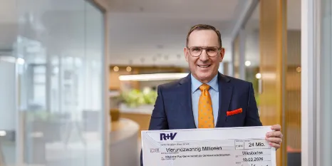 Jens Hasselbächer, Vorstand des Ressorts Kunden & Vertrieb der R+V Versicherung, mit einem symbolischen Cashback-Scheck über rund 24 Millionen Euro für die R+V-Mitglieder-Plus-Kunden