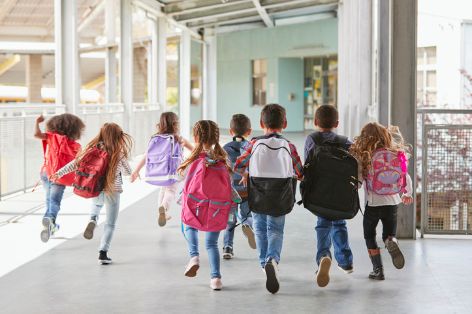 Kinder mit einem Ranzen auf dem Rücken laufen zum Unterricht als Symbol für die Erstausstattung für den Schulanfang.