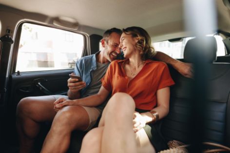 Mann und Frau lachen auf der Rückbank eines Autos.