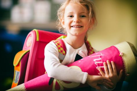 Ein Mädchen hält zum Schulbeginn eine mit Snacks und weiteren Überraschungen gefüllte Schultüte in der Hand.