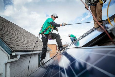Handwerker beim Installieren einer Photovoltaikanlage auf einem Hausdach.