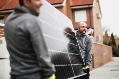 Zwei Männer tragen ein Solarpanel zur Baustelle für die Montage.