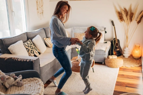 Mutter und Tochter springen gemeinsam im Wohnzimmer.