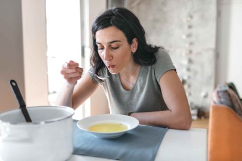 Ein Frau isst eine klare Gemüsesuppe.