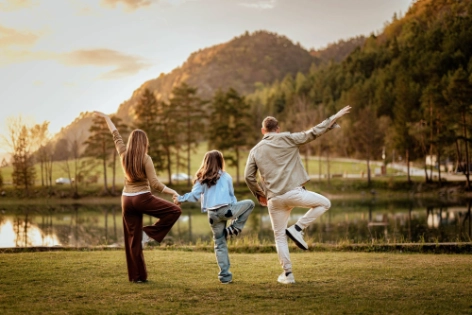 Familie macht Yoga im Freien, Mutter und Vater und Kind halten sich an den Händen.
