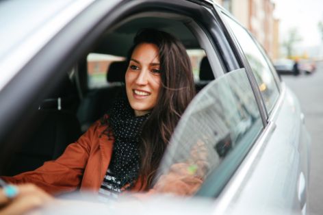 Frau fährt mit geöffnetem Autofenster durch die Stadt.