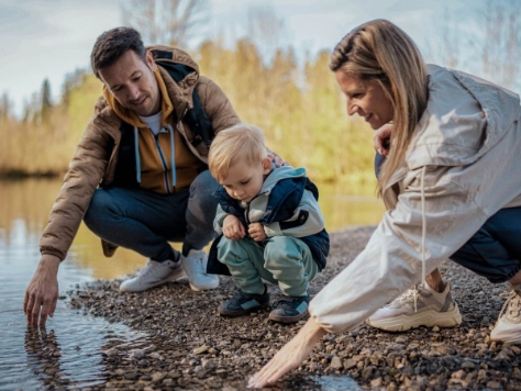Familie mit Kleinkind spielen am Rande eines Sees mit dem Wasser.