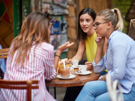 Drei junge Frauen sitzen im Cafe und diskutieren darüber, ob eine Berufsunfähigkeisversicherung sinnvoll ist.