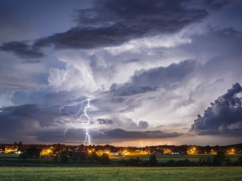 Ein Gewitter mit Blitzen über einer Ortschaft.