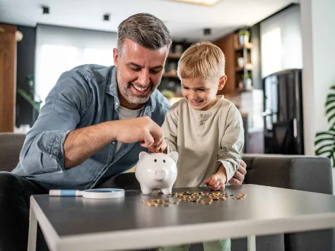 Ein Junge legt Münzen in ein Glas als Symbol für das Kindergeld, dass seine Eltern für ihn anlegen konnten. 