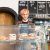 Junger Barista, der frisch zubereitete Speisen in der Auslage eines Cafés anrichtet.