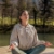 Frau im Trainingsoutfit sitzt am See und praktiziert Yoga.