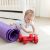 Ein Kleinkind krabbelt neben einer Yogamatte auf dem Fußboden und spielt mit einem Paar roter Hanteln