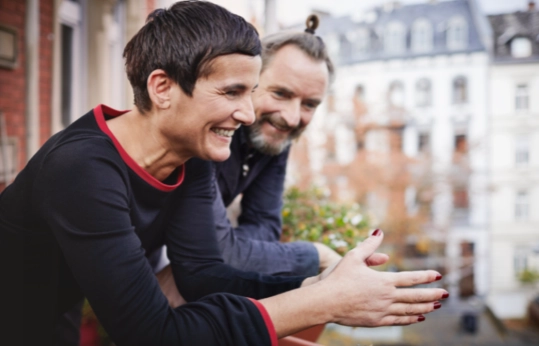 Zwei Männer lachen zusammen auf einem Balkon mit Blick auf alte Stadtgebäude im Hintergrund