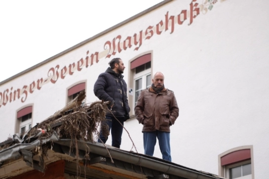 Zwei Männer stehen auf Holzbalken vor einem Gebäude mit der Aufschrift "Obst-Verein Mayschoss"