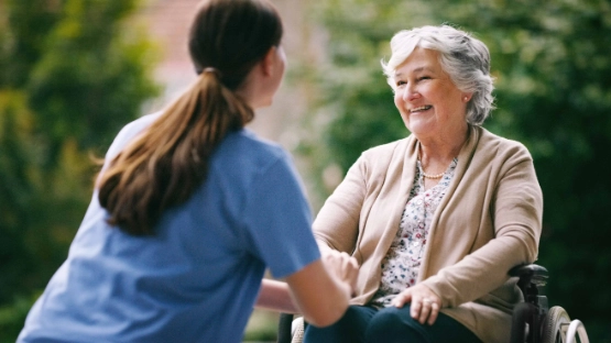 Lachende Seniorin im Rollstuhl mit Krankenschwester im Garten